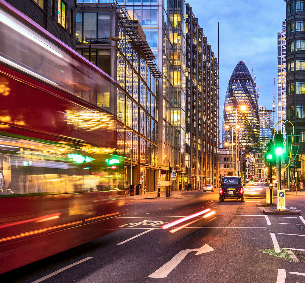 Financial district in London at dusk with buses driving through.