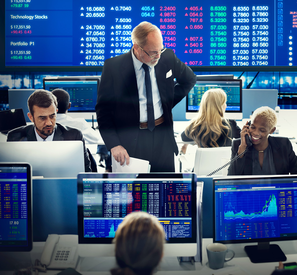 Business team investment trading in a monitoring room on desktops with screens showing stock market data.